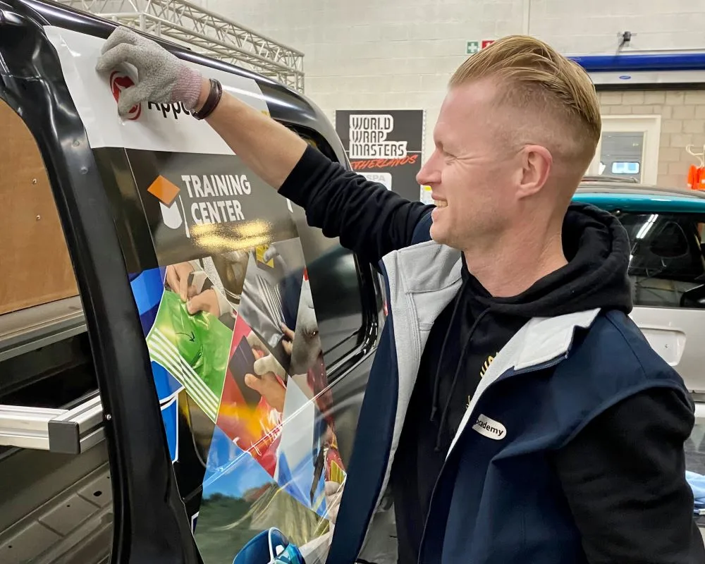 Trainer demonstreert hoe je printfolies en carwrapfolies moet inföhnen in diepe profileringen bij bedrijfswagens tijdens Appcademy signmaker training