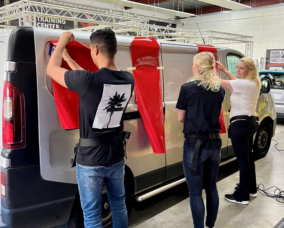 Cursisten plakken grote kleurvlakken zelfklevende folie op een bestelwagen tijdens de Appcademy signmaker cursus en beroepsopleiding