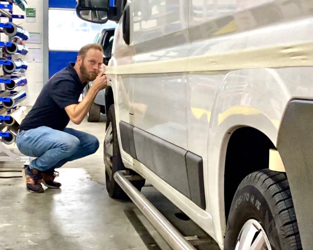 Een cursist oefent het uitzetten van een rechte baan of lijn met folie op de zijkant van een bestelbus tijdens de Appcademy opleiding signmaker training