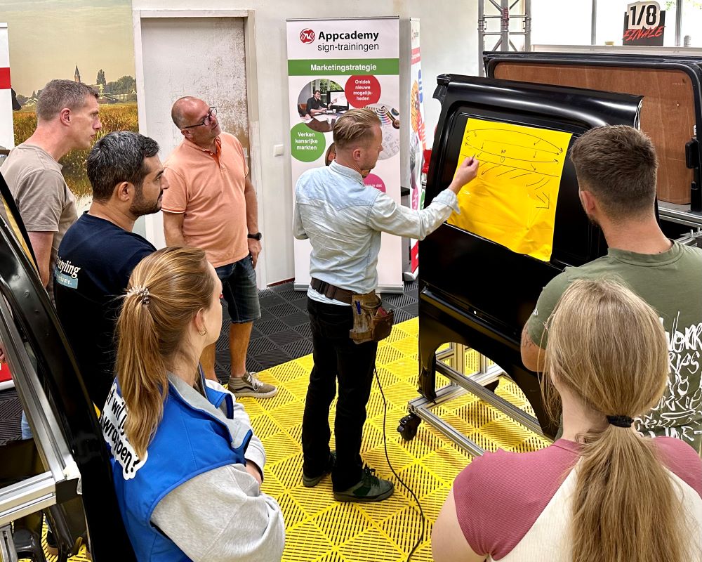 Trainer geeft instructie over de techniek van het plakken van zelfklevende folie tijdens de Appcademy signmaker cursus