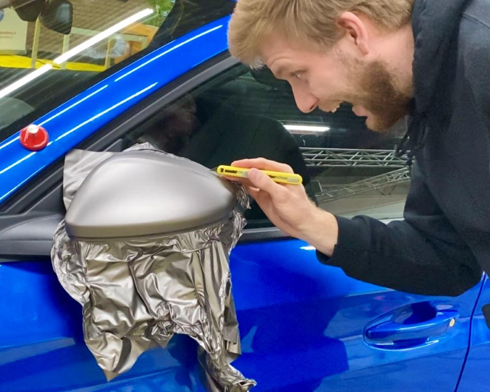 Cursist wrapt buitenspiegel van auto als praktijkoefening tijdens Appcademy carwrap workshop