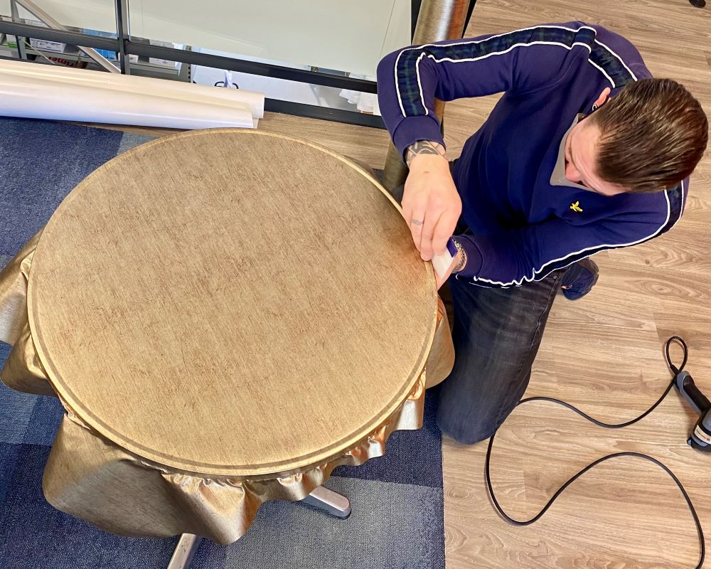 Cursist wrapt de bovenkant en zijkant van een bistro tafel als praktijkoefening tijdens de Appcademy training en opleiding interieurfolie plakken en keukens wrappen