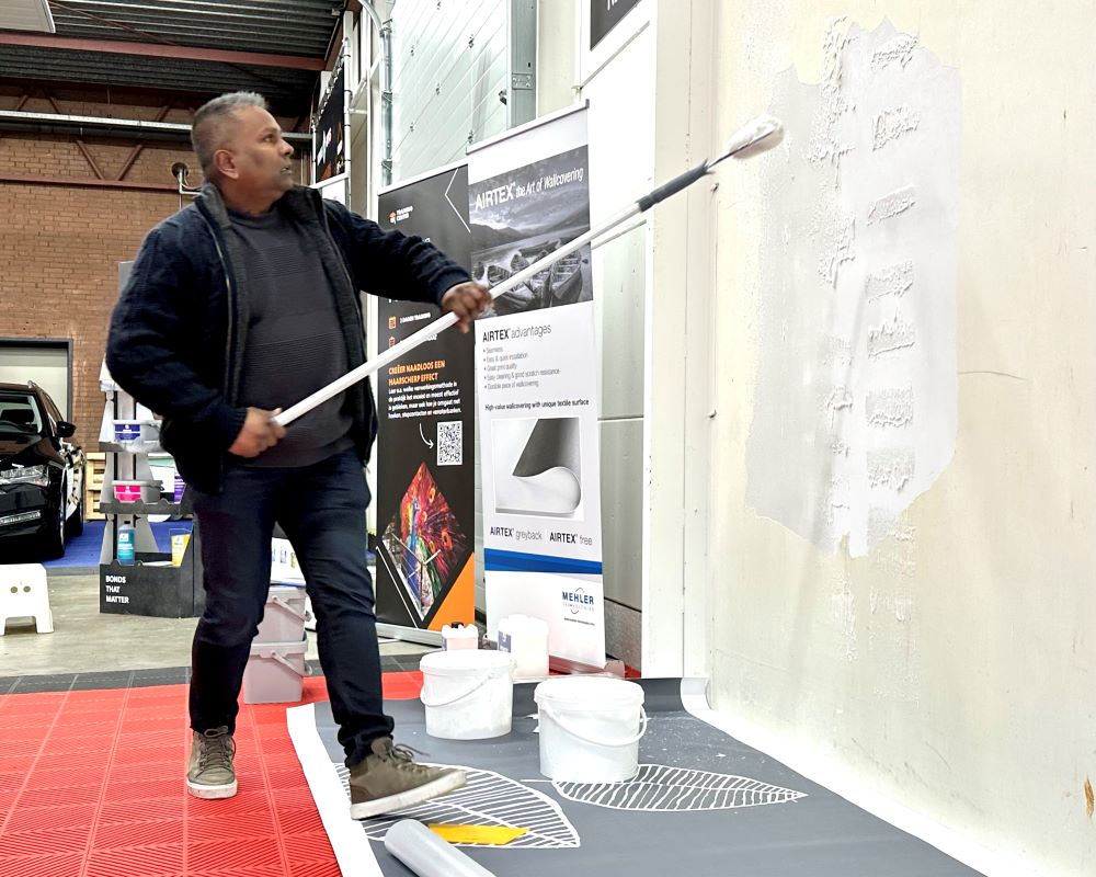 Trainer demonstreert het aanbrengen Flexx lijm voor Airtex en Walltex met een roller tijdens Appcademy Naadloos fotobehang training