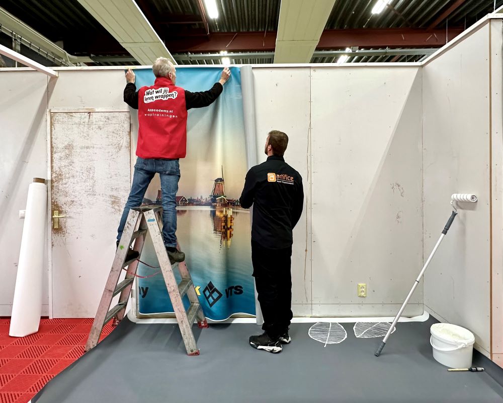 Cursisten plakken groot stuk naadloos fotobehang op wand tijdens Appcademy Naadloos fotobehang cursus