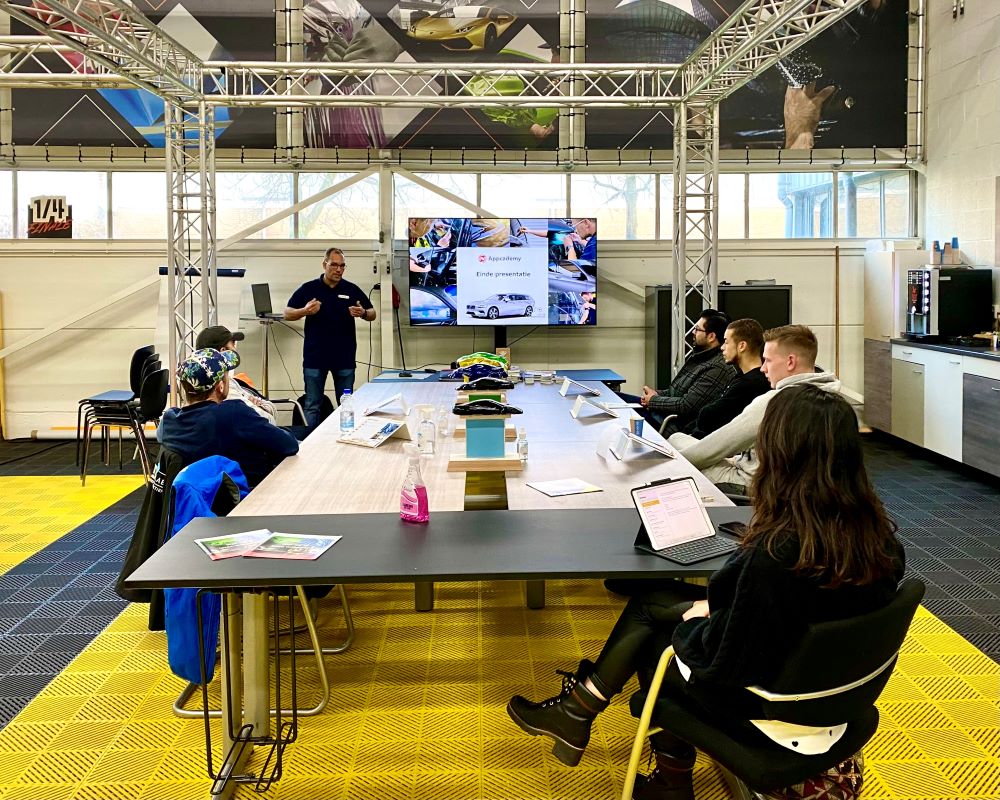 Trainer geeft info aan cursisten over raamfolie bij power point presentatie aan tafel tijdens Appcademy Automotive Windowfilm cursus