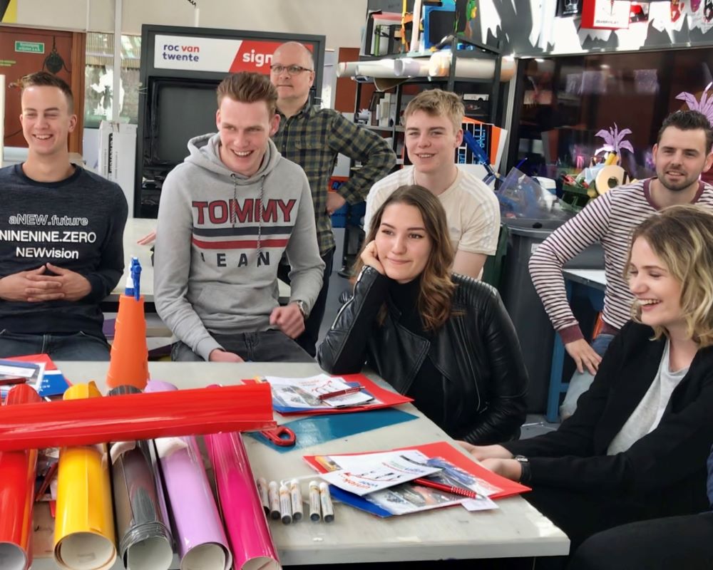Groep studenten en docent luisteren naar theorie informatie over plakken en wrappen tijdens Appcademy workshop en gastcollege op ROC / MBO opleiding signmaker