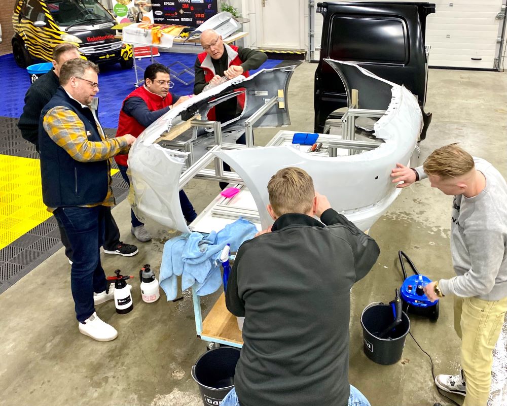 Trainer en groep cursisten plakken PPF op oefenbumpers van Porsche tijdens Appcademy Paint Protection Film training