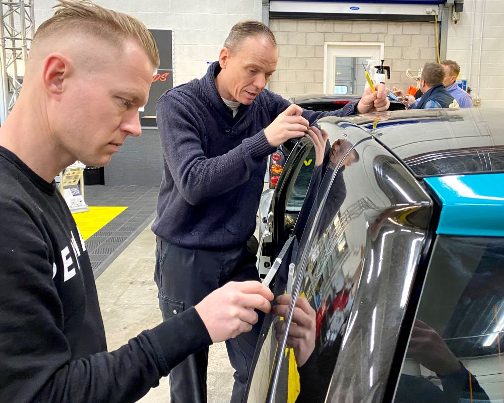 2 cursisten snijden als praktijkoefening strookjes PPF folie af op auto carosserie tijdens Appcademy Paint Protection Film training