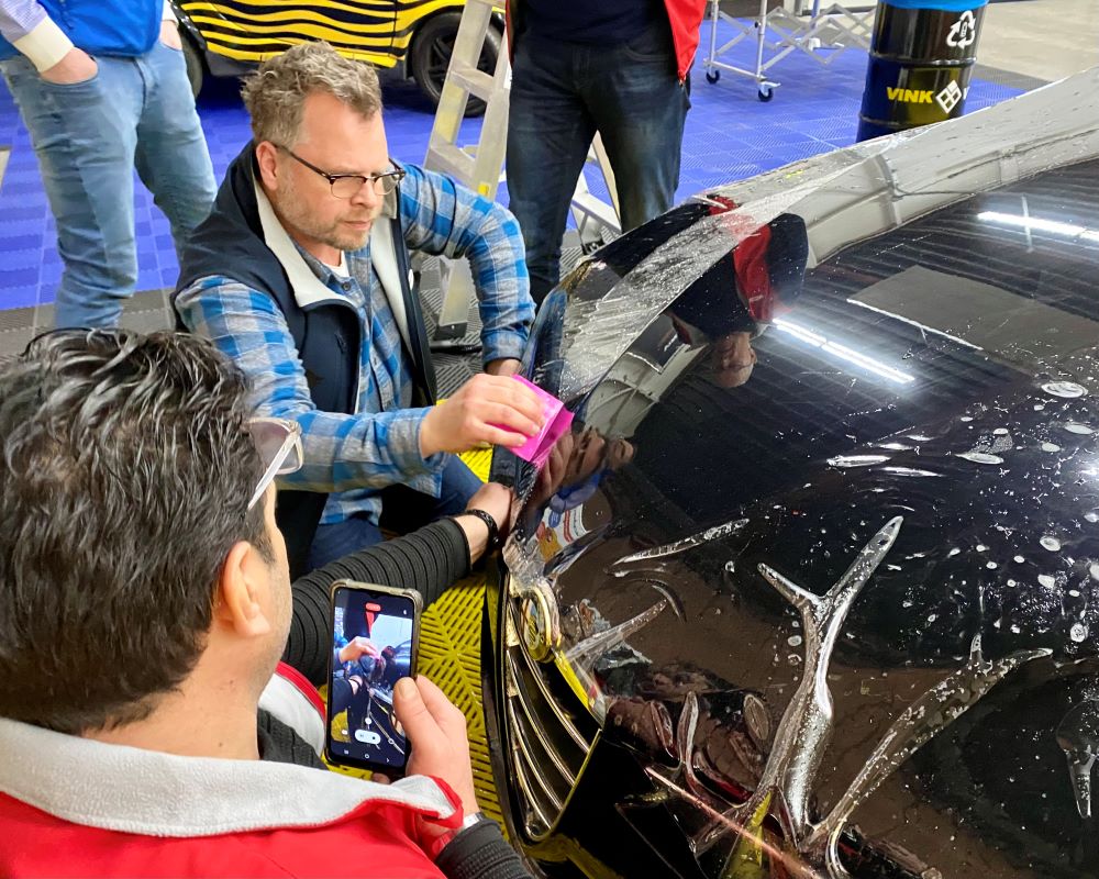 Trainer rakelt slip solution onder PPF op motorkap vandaan tijdens Appcademy Paint Protection Film cursus of opleiding