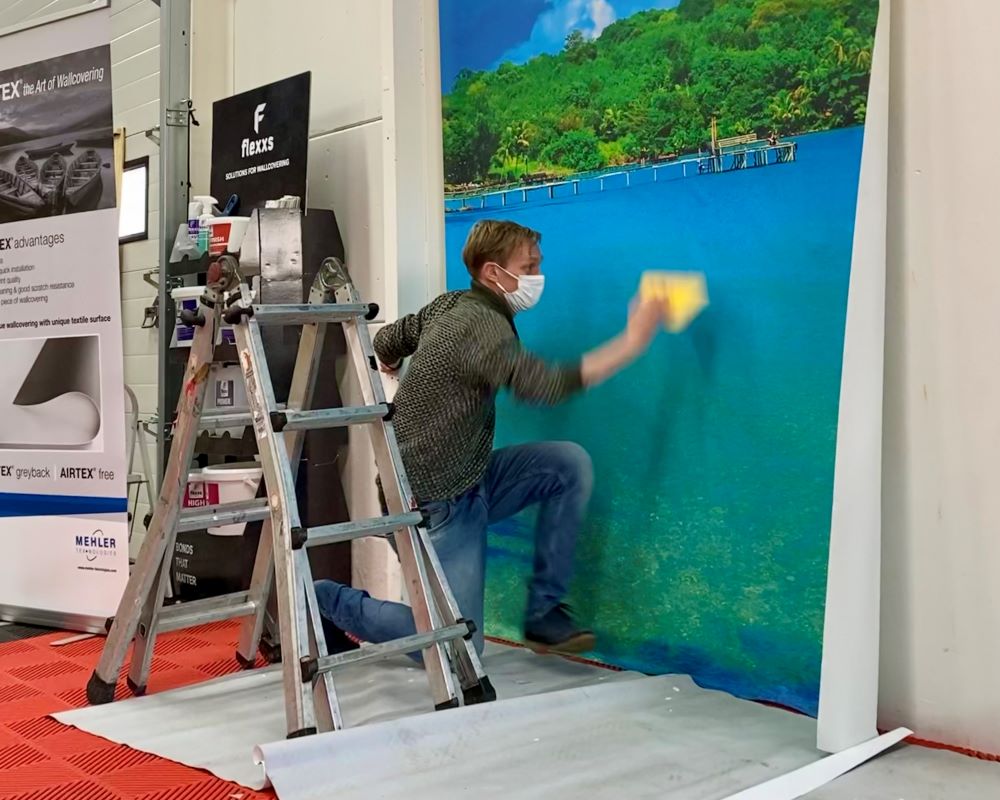 Trainer demonstreert aan cursisten hoe hard je moet duwen met je rakel op de behanglijm onder fotobehang tijdens Appcademy Naadloos fotobehang cursus