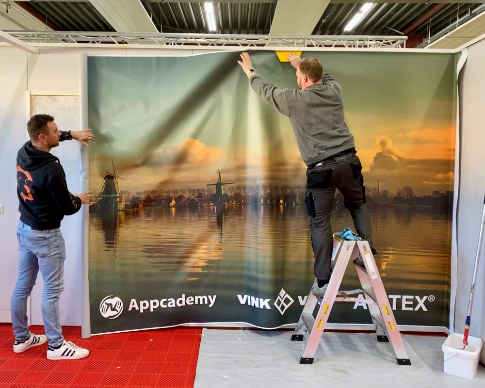 Cursisten plakken samen groot formaat naadloos fotobehang op wand tijdens Appcademy Naadloos fotobehang training