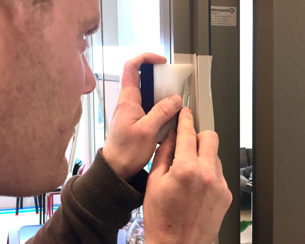 Cursist beplakt binnenhoek van een kozijn met Facadefilm kozijnfolie tijdens Facadefilm opleiding cursus “Schilderen met folie”