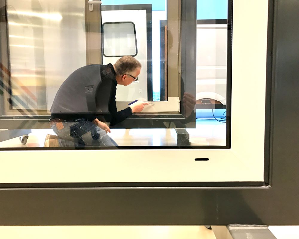 Cursist plakt Facadefilm kozijnfolie met rakel vast op aluminium kozijn tijdens “Schilderen met folie” Facadefilm training