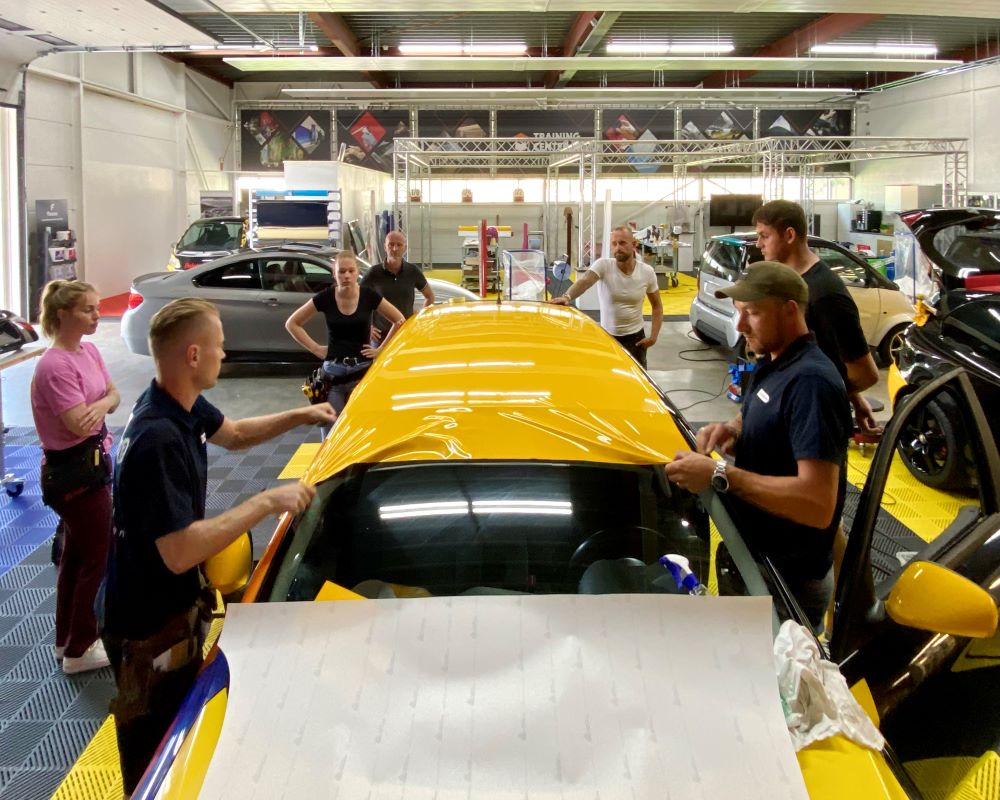 Praktijkoefening: Cursisten en trainer wrappen dak van auto tijdens Appcademy carwrap opleiding