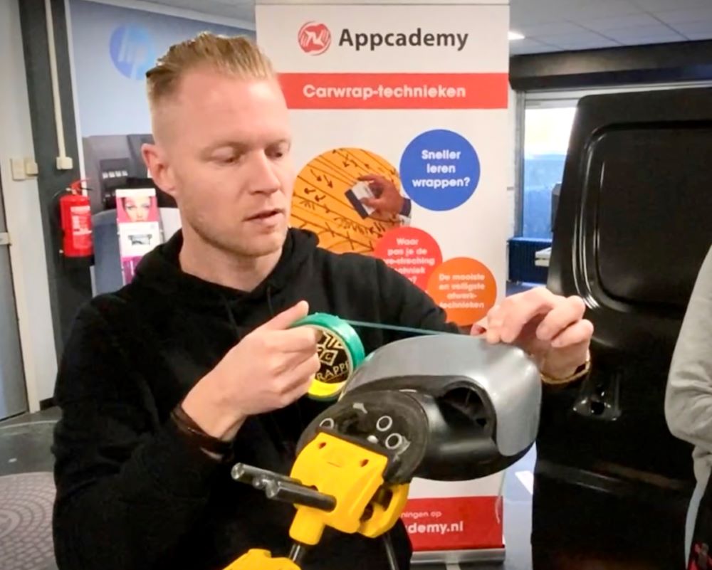 Trainer demonstreert knifeless tape tijdens wrappen van buitenspiegel tijdens Appcademy carwrap cursus
