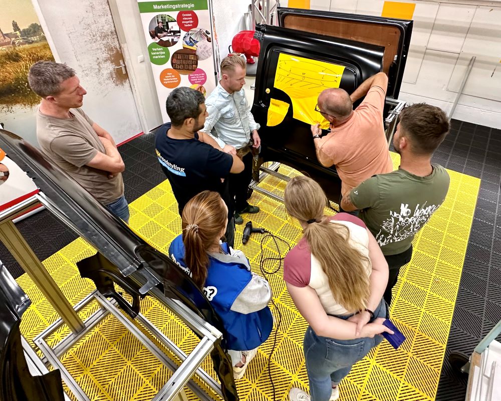 Trainer bespreekt met cursisten hoe je zelfklevende folie professioneel aanrakelt of aanwrijft tijdens de Appcademy signmaker advanced workshop