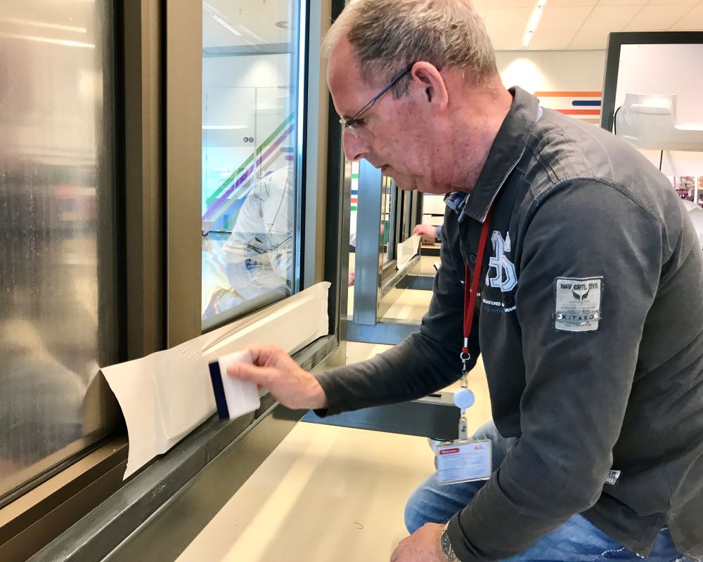 Cursist brengt Facadefilm kozijnfolie met rakel tool aan op aluminium kozijn tijdens “Schilderen met folie” Facadefilm training