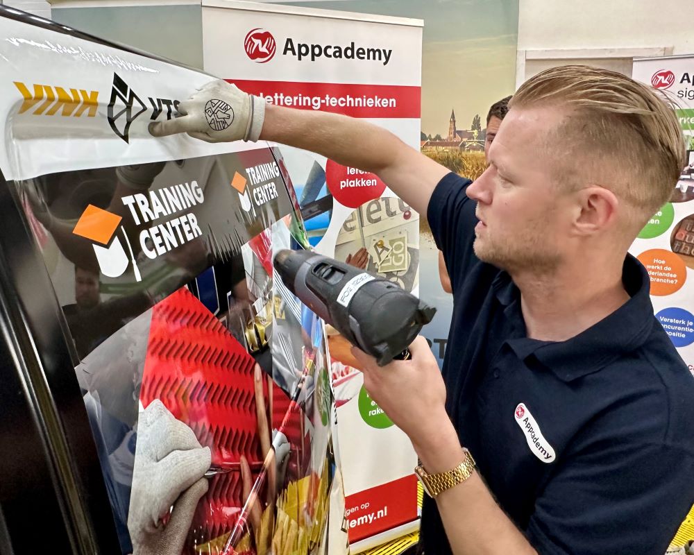 Trainer demonstreert hoe je printfolie in een diep profiel wrapt tijdens de Appcademy signmaker advanced workshop
