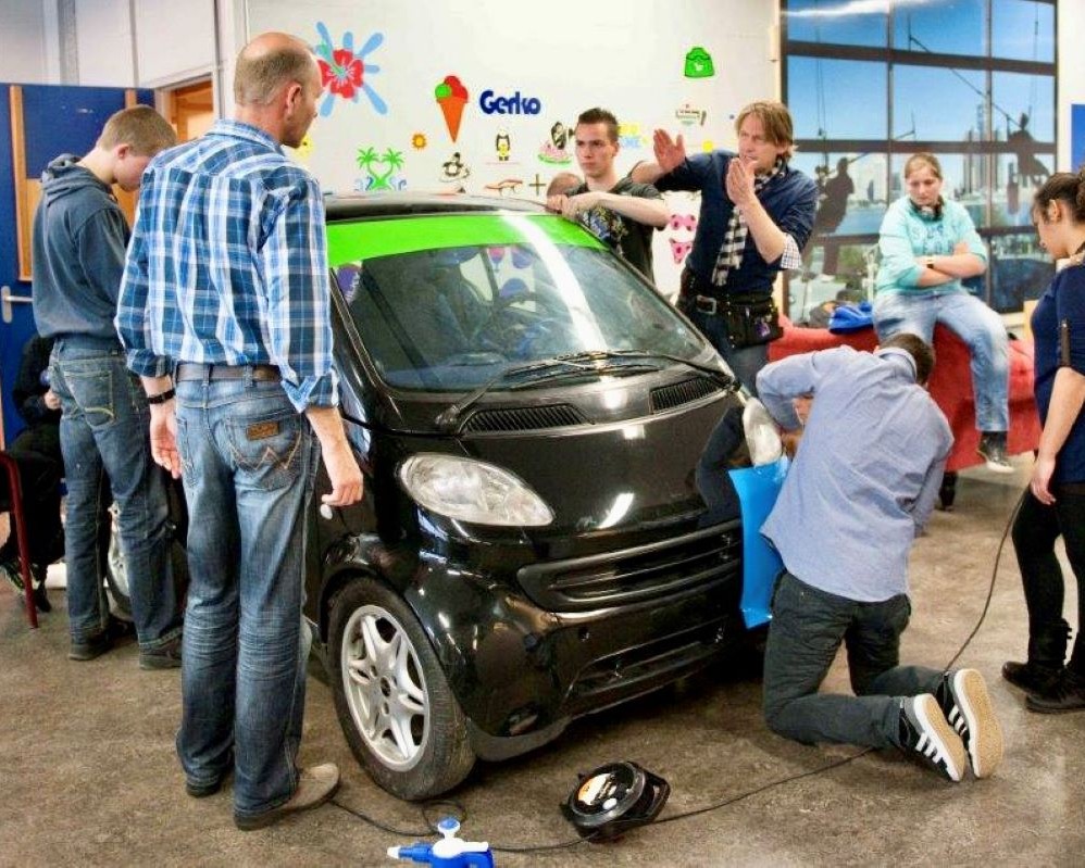 Trainer geeft aanwijzingen folie voor wrappen en plakken aan studenten en docent van de school tijdens Appcademy workshop en gastcollege op ROC / MBO signopleiding