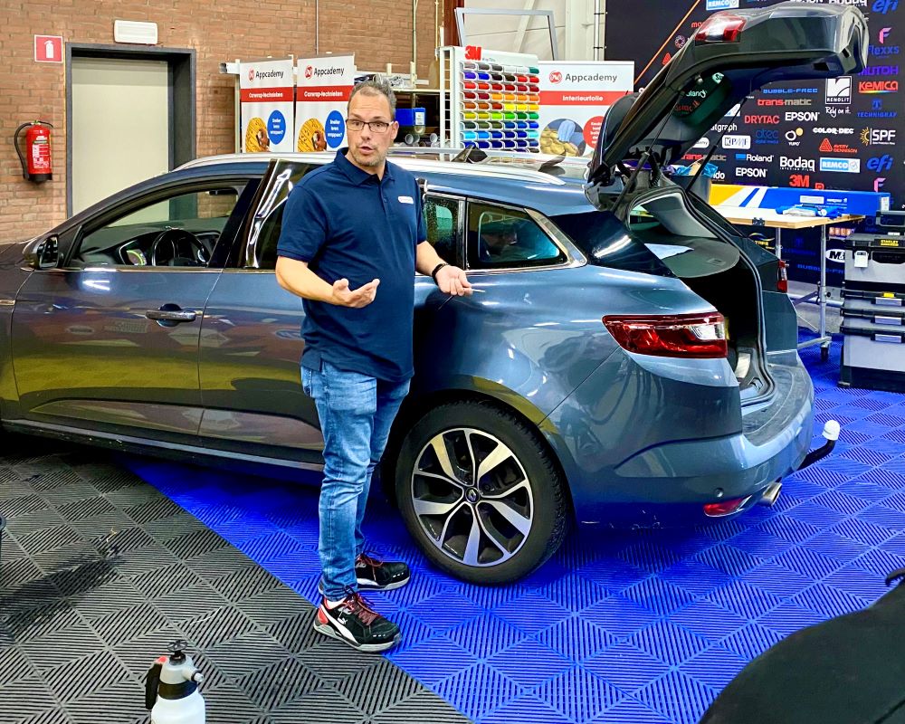 Trainer geeft uitleg over appliceren van raamfolie bij demo voertuig presentatie tijdens Appcademy Automotive Windowfilm cursus