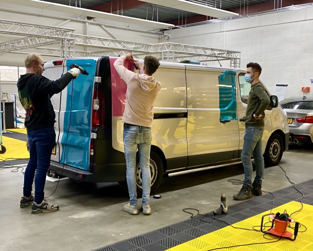 Cursisten brengen grote vlakken kleurfolie aan op bedrijfsbus met complexe ondergronden tijdens de Appcademy signmaker advanced training